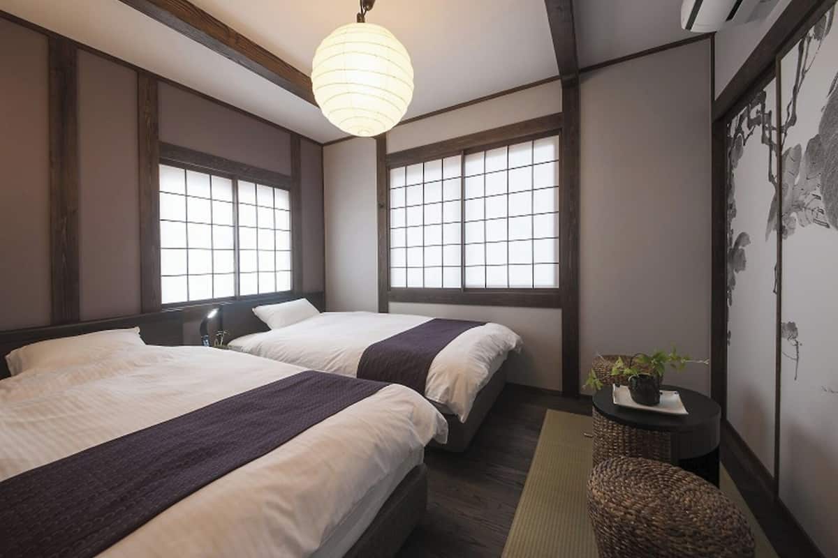 A traditional Japanese-style room with two beds, a hanging light fixture, and a view of the outside through shoji screens.