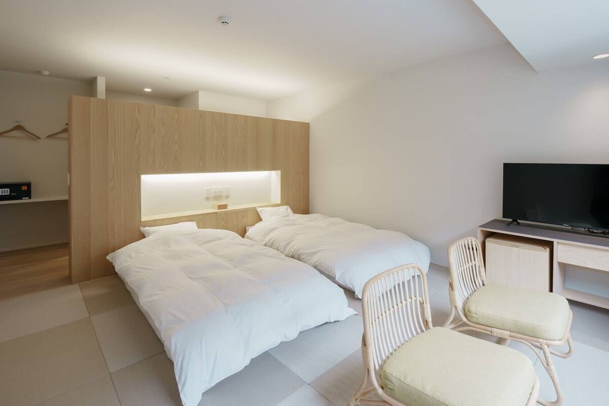 Ein modernes Hotelzimmer mit zwei Betten, einem Fernseher, einem Schreibtisch und einem Sessel.