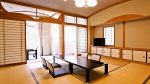 A traditional Japanese room with tatami flooring, a low table with cushions, sliding doors, and a television on a shelf. - Mimata Onsen Nagomi Yuyado Kanagi (Hamada)