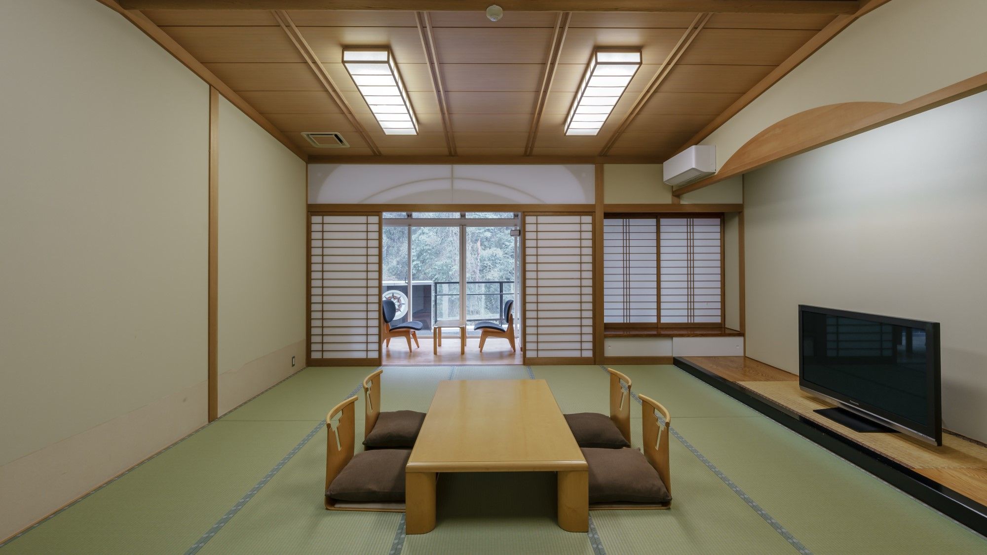 A traditional Japanese room with tatami flooring, a low table with cushions, sliding doors, and a television.