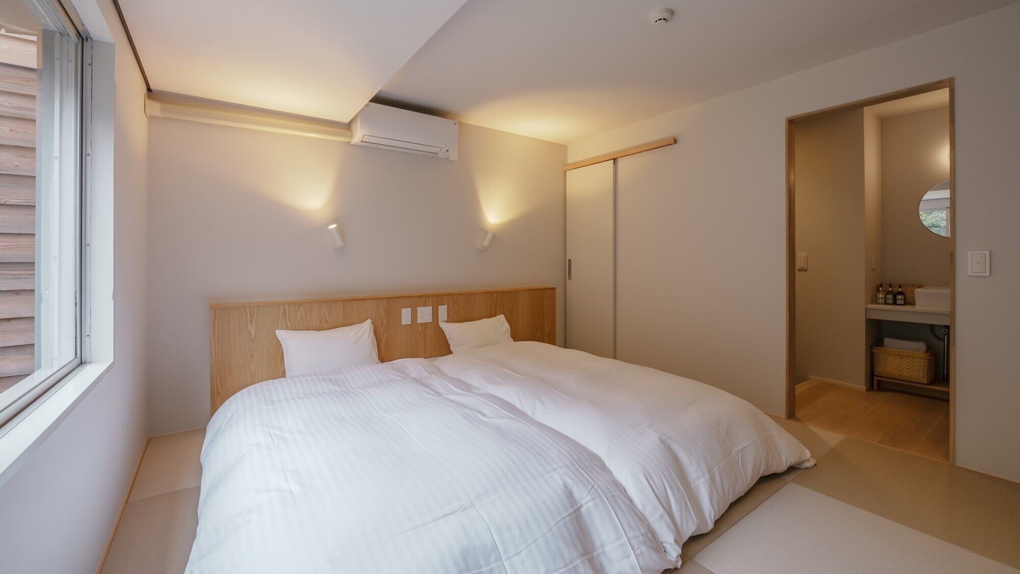 A bedroom with a large bed, a window, an air conditioning unit, and a closet.