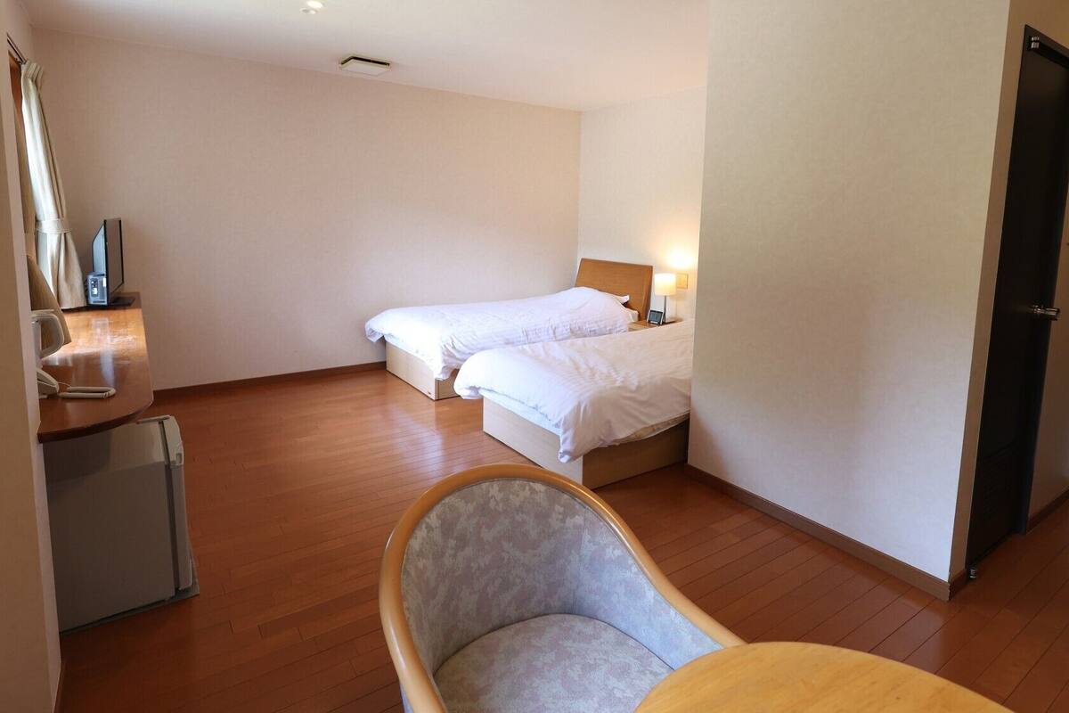 Ein Hotelzimmer mit zwei Einzelbetten, einem kleinen Schreibtisch mit Telefon, einem Stuhl und einer Tür.