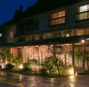 A two-story building with a covered entrance and a garden area with trees.