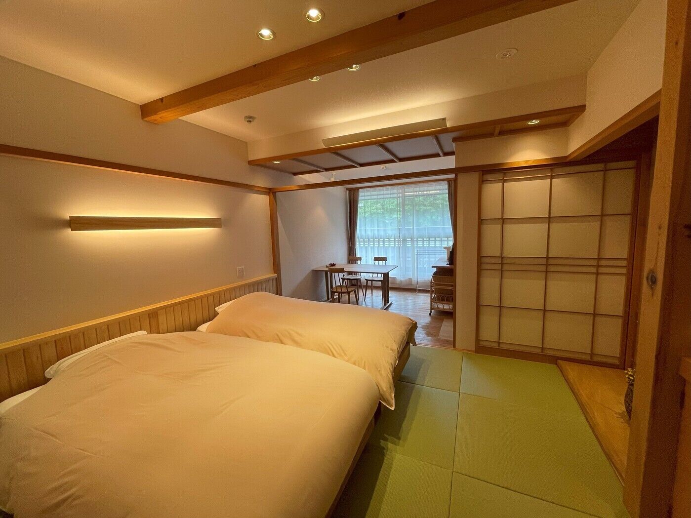 A room with two beds, a small table, and a sliding door.