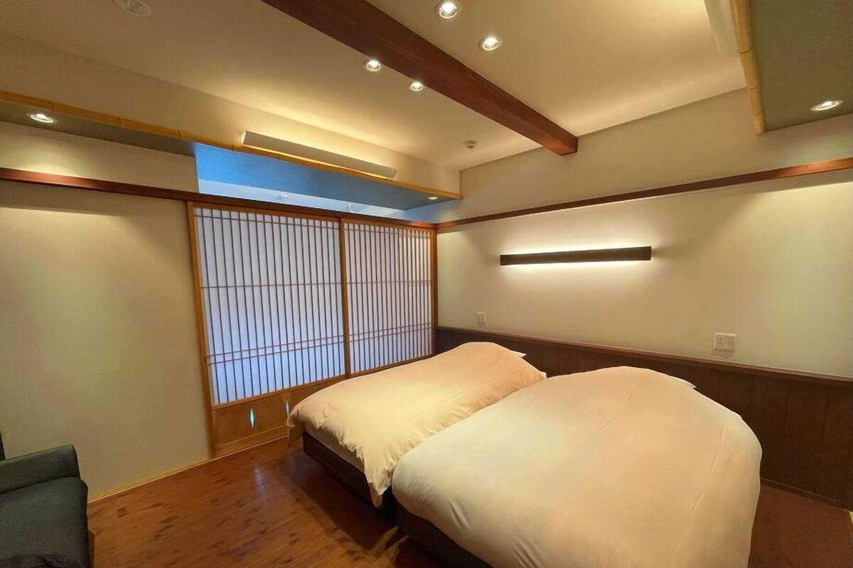 A room with a wooden floor, two beds with white bedding, a shoji screen, and recessed ceiling lighting.
