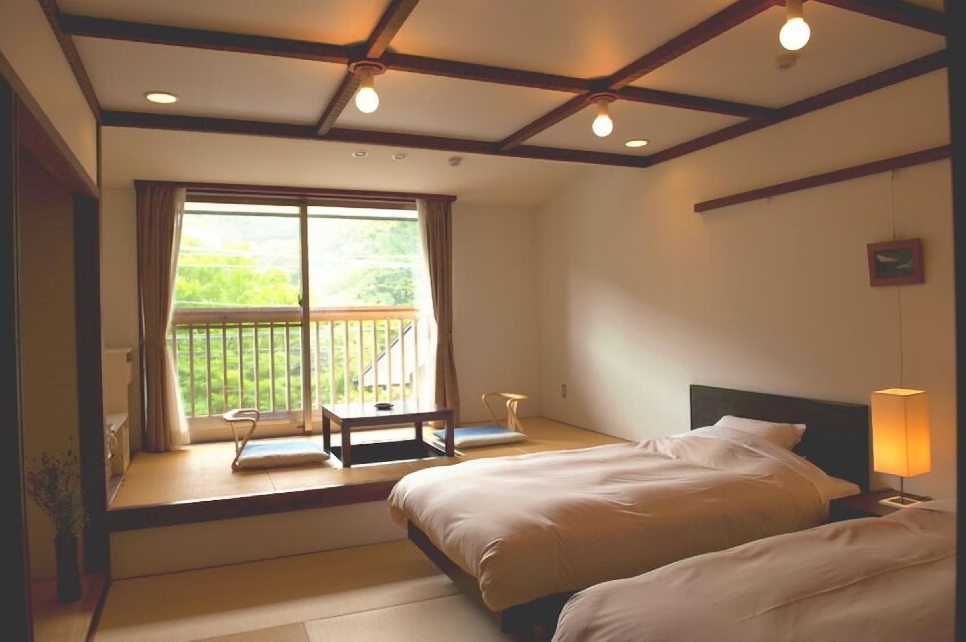 A hotel room with a bed, a small table, a chair, a lamp, and a balcony with a view.