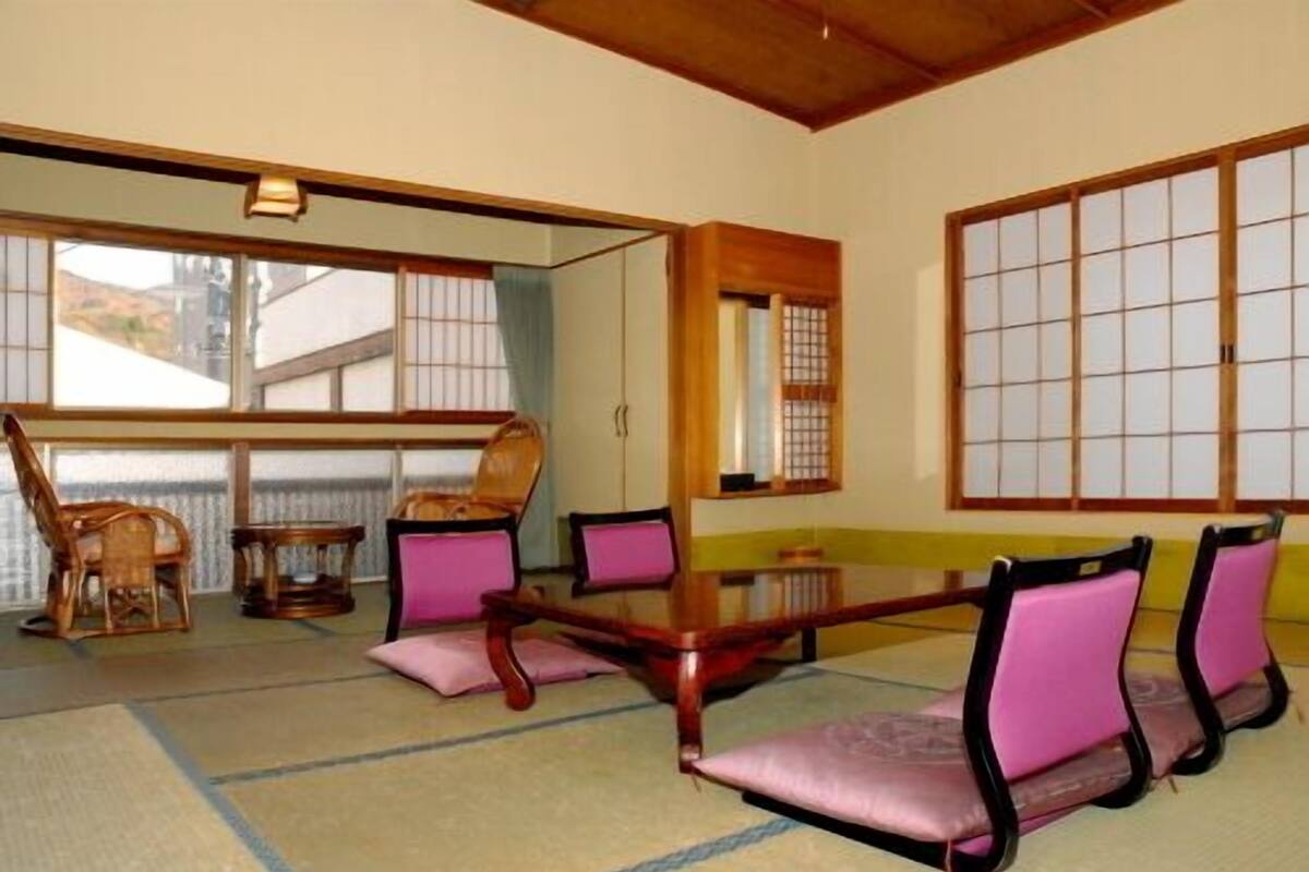 Um quarto japonês tradicional com tatames, uma mesa baixa e cadeiras de madeira com almofadas.