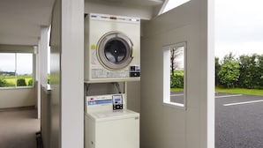 A laundry facility with a washing machine and dryer, a control panel, and a window providing a view of the parking lot and greenery. - Family Lodge Hatagoya Mito Oarai (Mito)