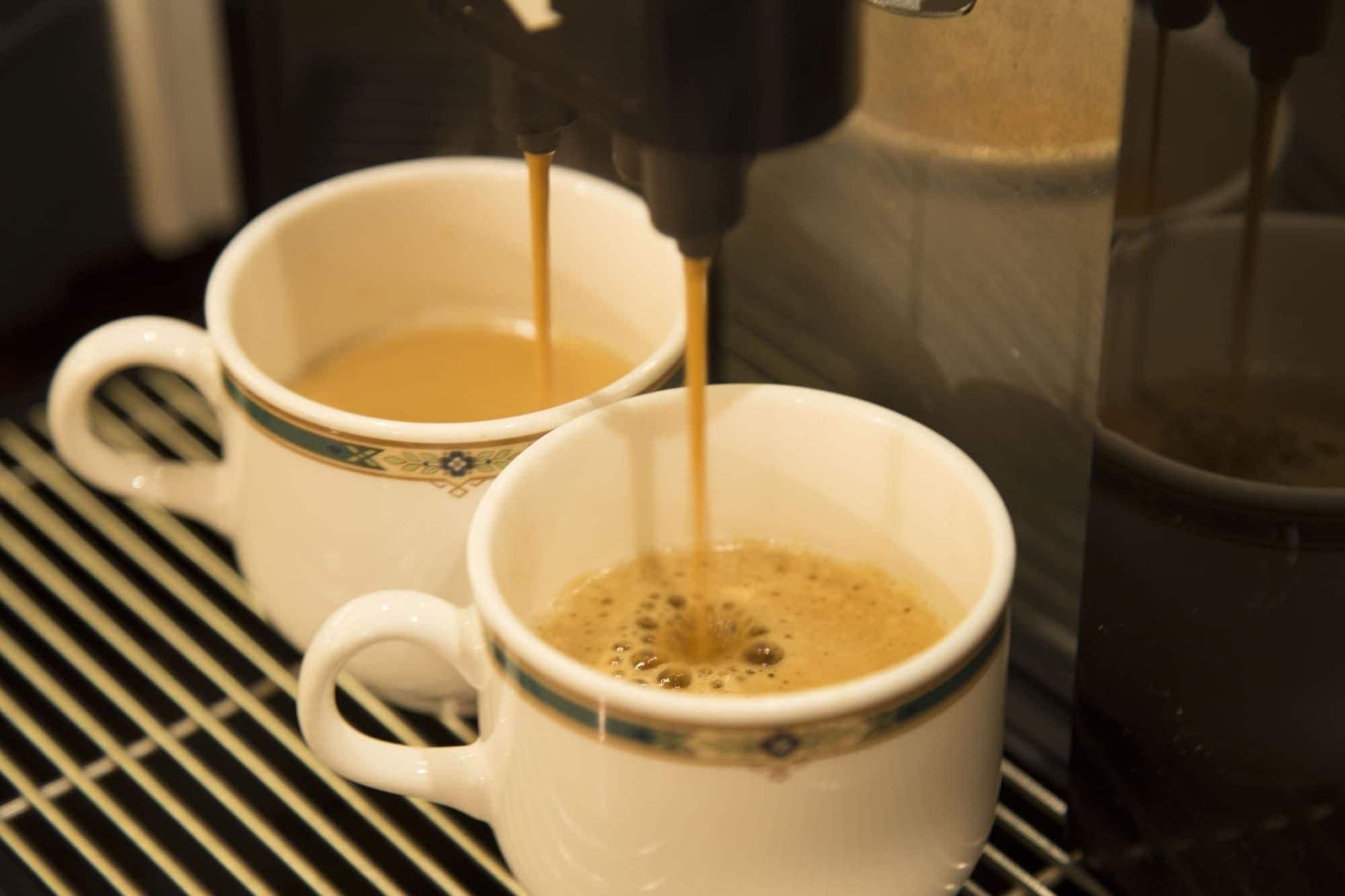 Dos tazas blancas de café sobre un estante metálico.