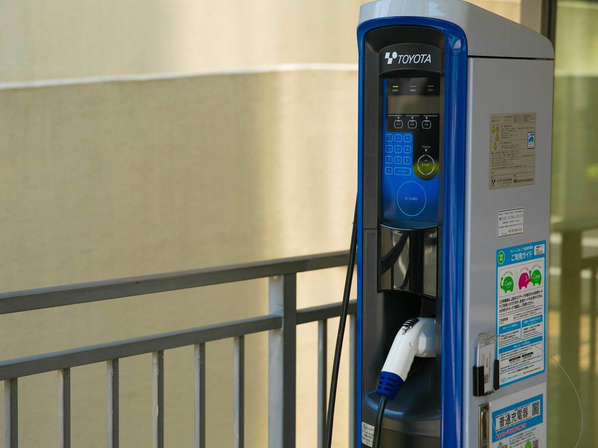 A Toyota electric vehicle charging station with a digital display, charging cable, and informational stickers.
