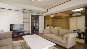 A modern living room with a sofa, a coffee table, a TV, and a sliding door leading to another room. - Hotel Showa Club (Atami)