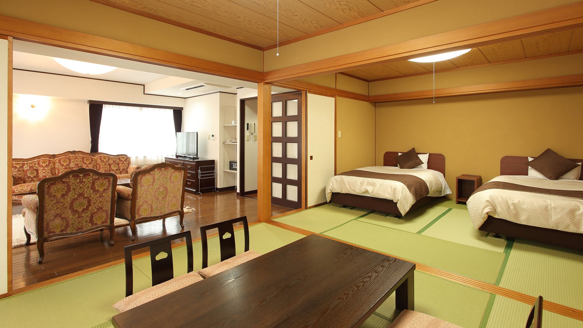 A traditional Japanese-style hotel room with tatami flooring, a low wooden bed, a sofa, and a dining table.