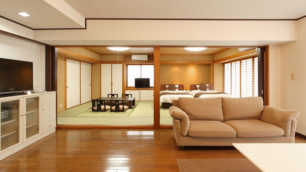 A traditional Japanese-style room with tatami flooring, a tatami mat area, a sofa, a television, and a bed with futons.
