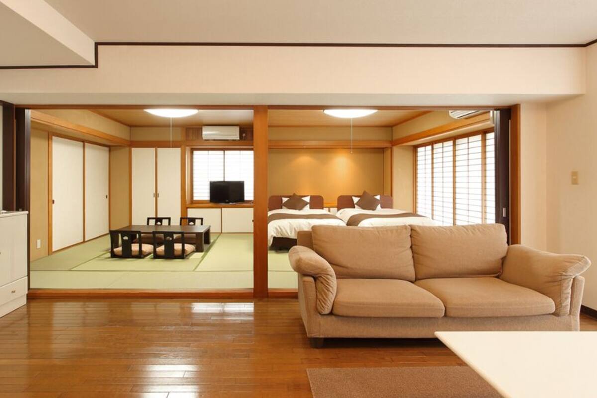 Una tradizionale stanza in stile giapponese, con pavimento in tatami, un'area in tatami, un divano, una televisione e un letto con futon.