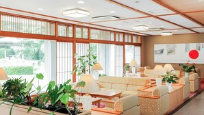 A hotel lobby with a traditional Japanese aesthetic, featuring tatami flooring, low wooden tables, and a large window with a view of greenery. - Ichinomata Onsen Grand Hotel (Shimonoseki)