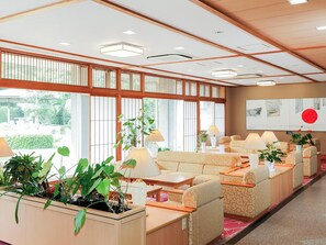A hotel lobby with a traditional Japanese aesthetic, featuring tatami flooring, low wooden tables, and a large window with a view of greenery. - Ichinomata Onsen Grand Hotel (Shimonoseki)