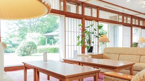 A traditional Japanese-style room with tatami flooring, a low wooden table, a sofa, and a potted plant. - Ichinomata Onsen Grand Hotel (Shimonoseki)