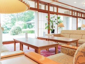 A traditional Japanese-style room with tatami flooring, a low wooden table, a sofa, and a potted plant. - Ichinomata Onsen Grand Hotel (Shimonoseki)