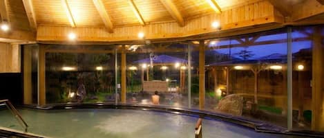 An indoor swimming pool with a wooden ceiling and glass walls.