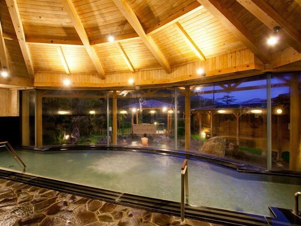 Une piscine intérieure dotée d’un plafond en bois et de murs en verre.