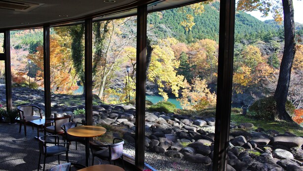 Una habitación con amplias ventanas que dan a un paisaje rocoso y un río, amueblada con mesas y sillas.