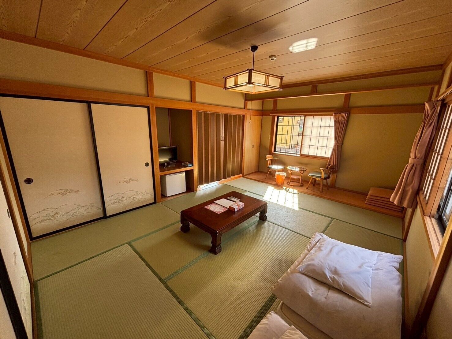 Una habitación japonesa tradicional con suelo de tatami, una mesa de madera baja, un sofá, puertas correderas y un televisor.