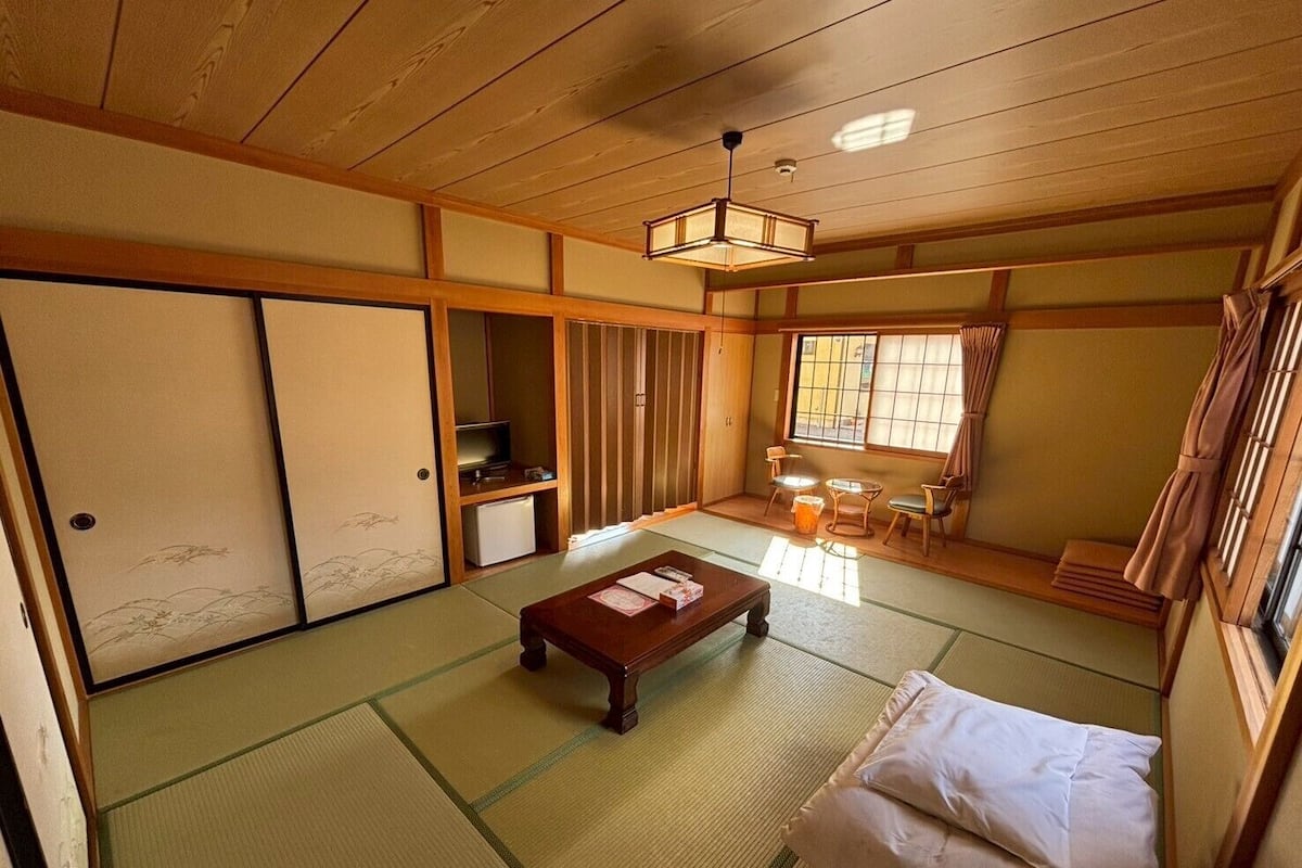 Une pièce de style japonais traditionnel, avec un sol recouvert de tatamis, une basse table en bois, un canapé, des portes coulissantes et un téléviseur.