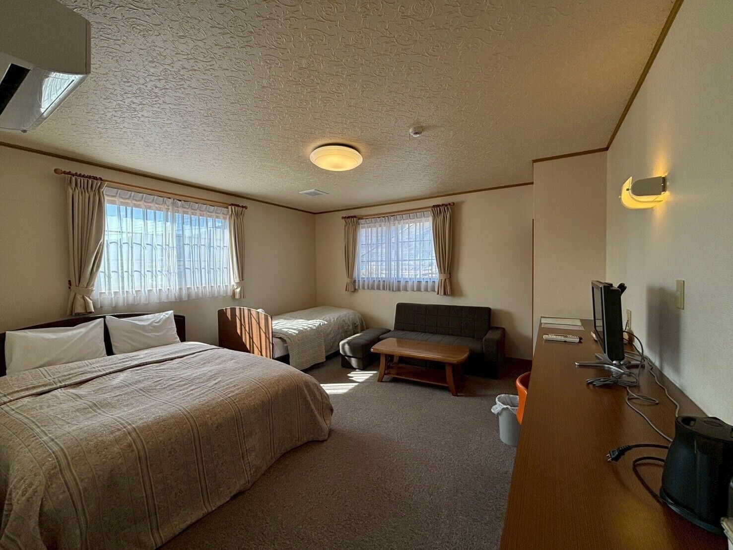 Habitación de hotel con dos camas, un sofá, un escritorio con computadora y un televisor.