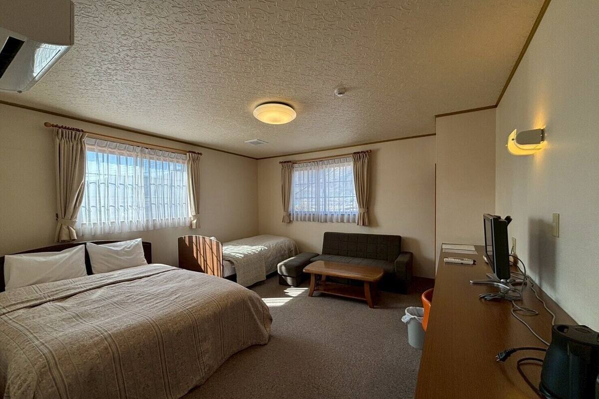 Une chambre d’hôtel avec deux lits, un canapé, un bureau avec un ordinateur et une télévision.