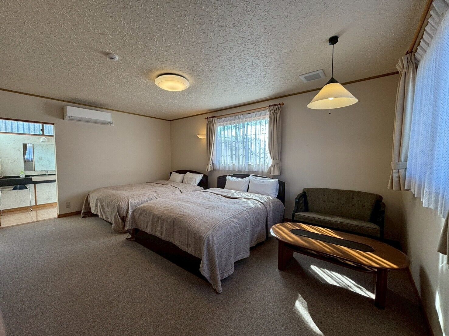 Un dormitorio con dos camas, una mesita, una silla, un espejo y una ventana con cortinas.