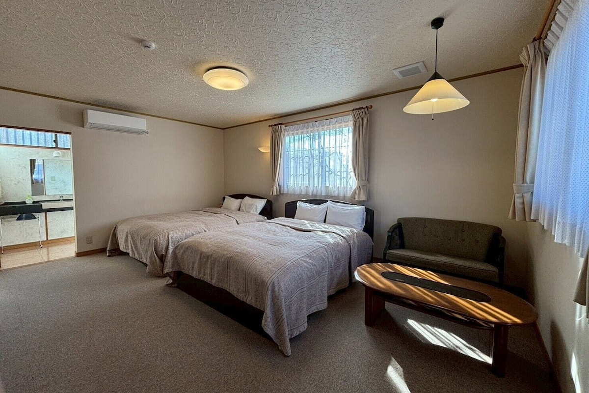 Une chambre avec deux lits, une petite table, une chaise, un miroir et une fenêtre avec des rideaux.