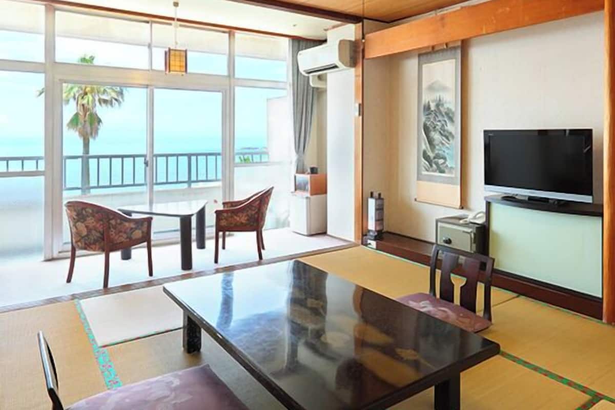 Una habitación con un gran ventanal, una mesa de comedor, sillas, un televisor y un mueble pequeño.