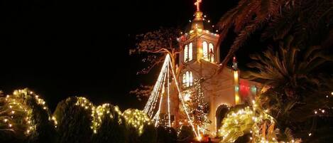 Igreja com cruz no topo, cercada por árvores e luzes.