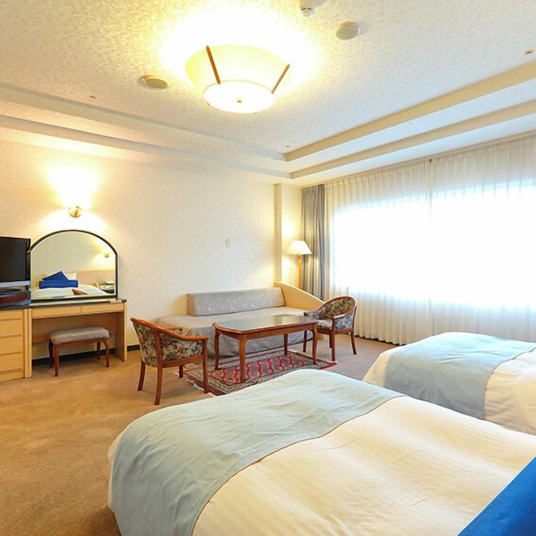 Una habitación de hotel con un escritorio, dos sillas, un sofá y dos camas.