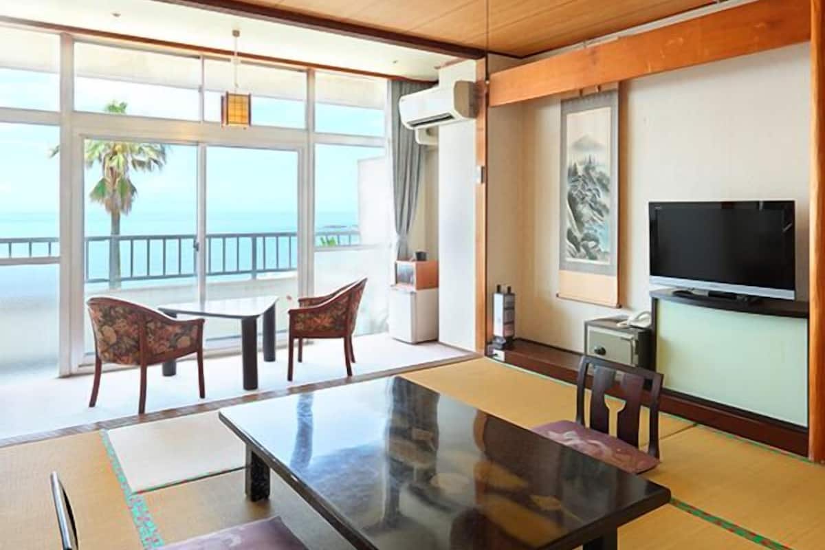 Una habitación con un ventanal grande, una mesa de comedor, sillas, un televisor y un futón.