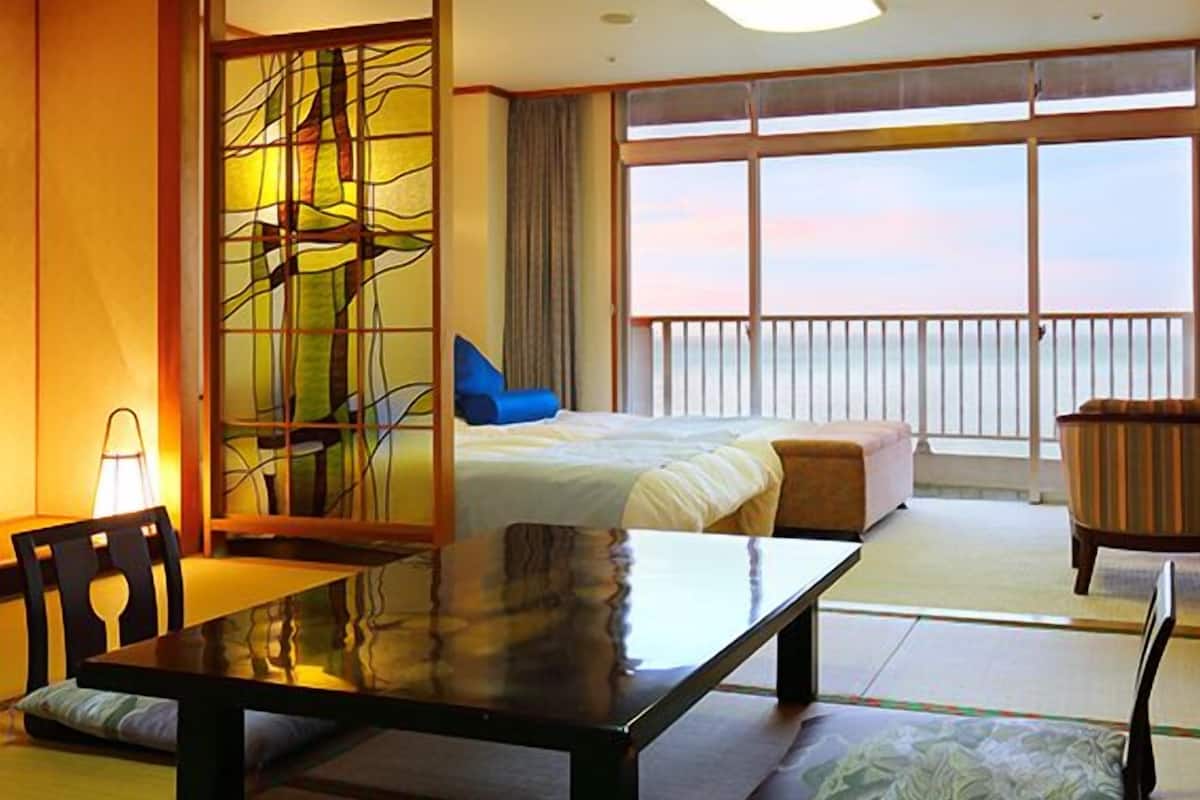 Un cuarto de hotel con una cama, una mesa de comedor, una silla, un sofá y vista al mar.
