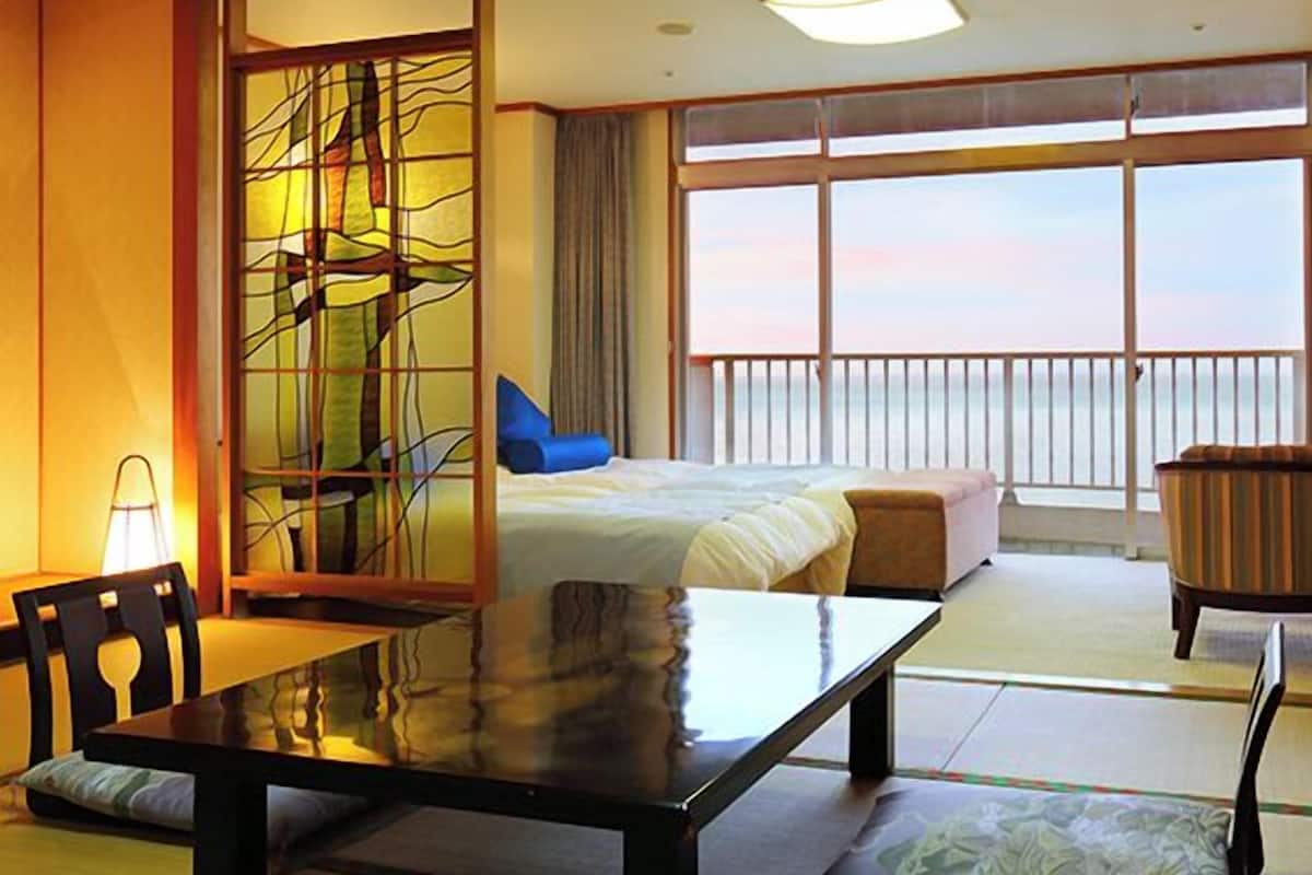 Habitación de hotel con cama, mesa de comedor, una silla, un sofá y vistas al mar.