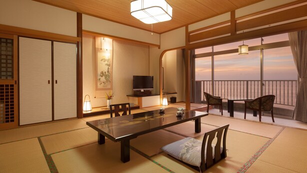 A traditional Japanese room with tatami flooring, a low table, chairs, a television, and a view of the sea. - Boyokaku (Amakusa)
