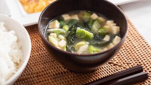 A bowl of soup with tofu and green vegetables, accompanied by a plate of rice and various other dishes. - Super Hotel Hachinohe Natural Hot Springs (Hachinohe)