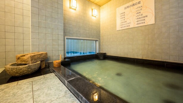 A traditional Japanese onsen with a stone basin, a wooden bench, and a wall-mounted clock. - Super Hotel Hachinohe Natural Hot Springs (Hachinohe)