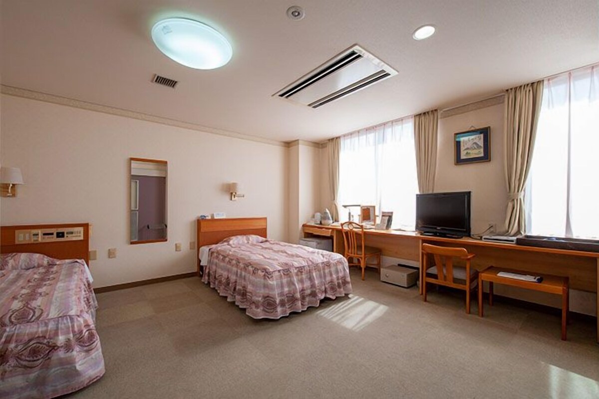 Une chambre d’hôtel avec deux lits, un bureau avec un ordinateur, une télévision et une fenêtre avec des rideaux.