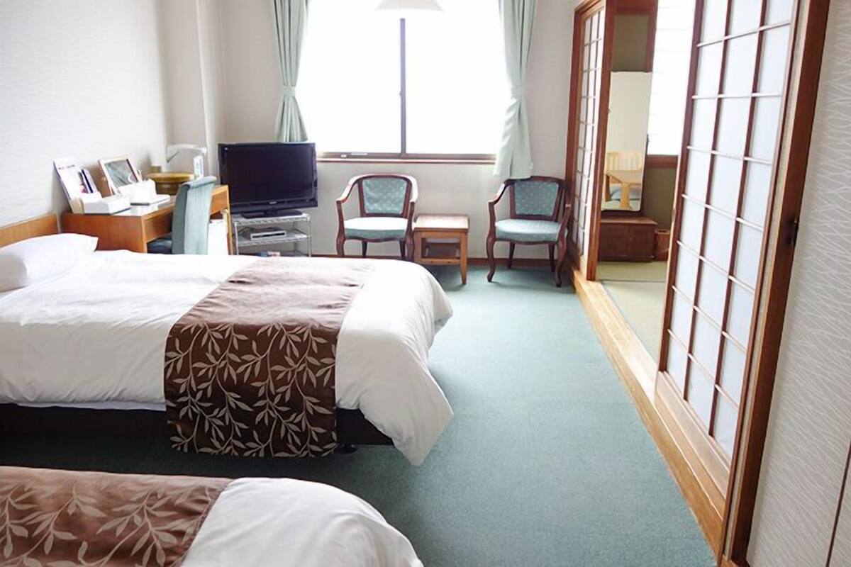 Une chambre d’hôtel avec deux lits, une télévision, un bureau avec une chaise et une porte coulissante.