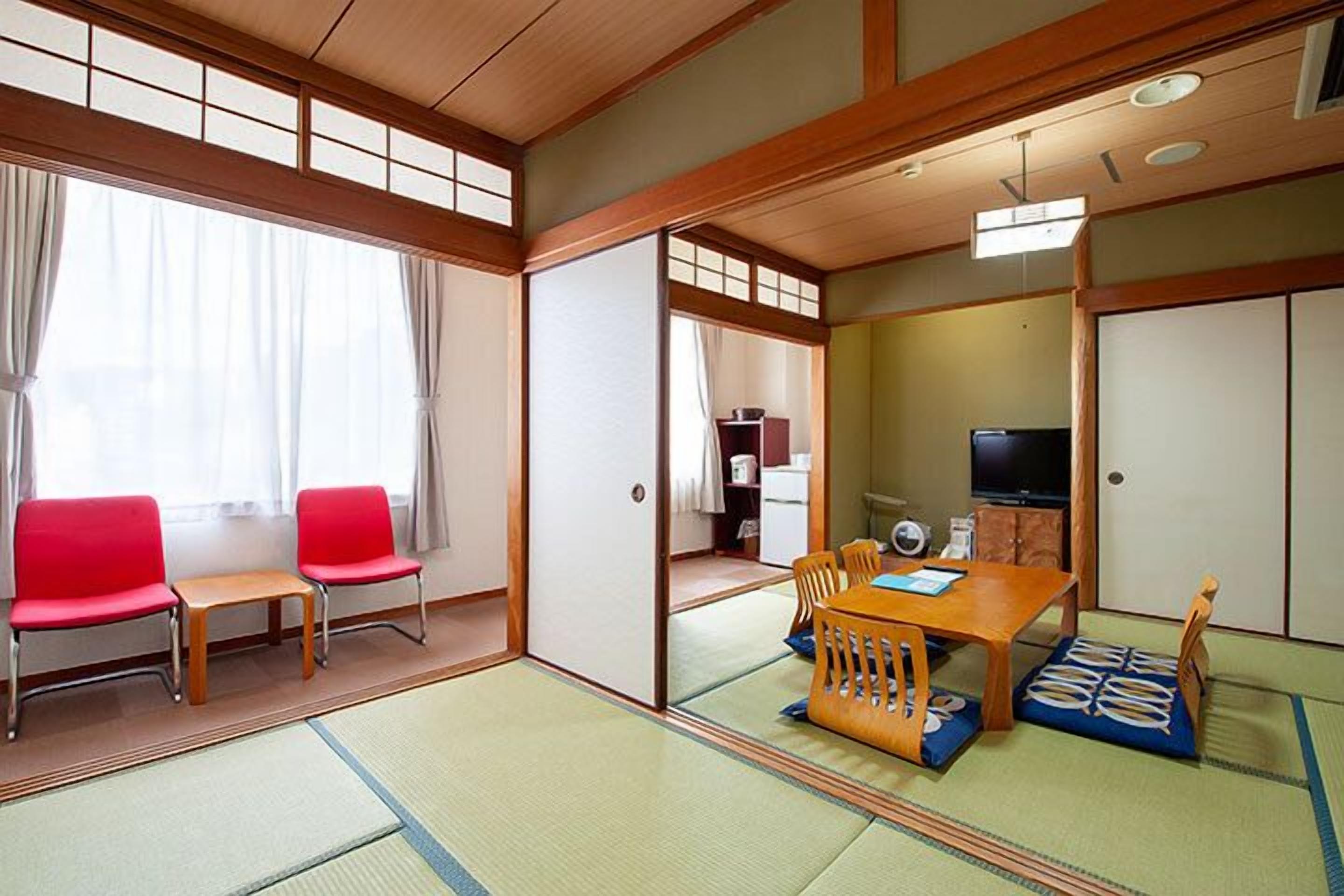 A traditional Japanese room with tatami flooring, a low wooden table, red chairs, and a television.