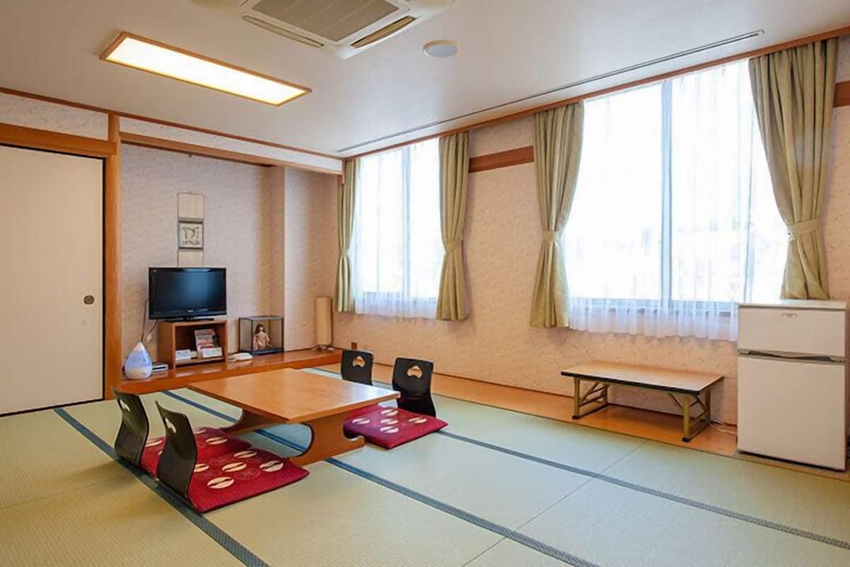 A traditional Japanese room with tatami flooring, a television, a small refrigerator, and a window with curtains.
