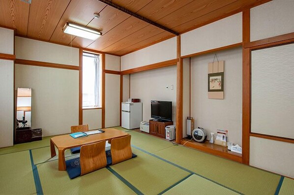 A traditional Japanese room with tatami flooring, a wooden table, a television, and a refrigerator. - Nigitatsu Kaikan (Matsuyama)