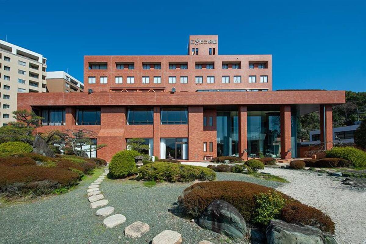 A modern building with a red brick facade, large windows, and a well-maintained garden with stepping stones and shrubs.