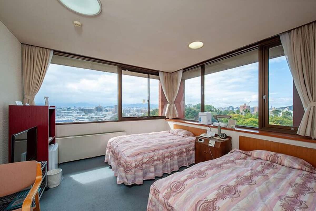 Une chambre d’hôtel avec deux lits, un bureau, une télévision et de grandes fenêtres donnant sur la ville.