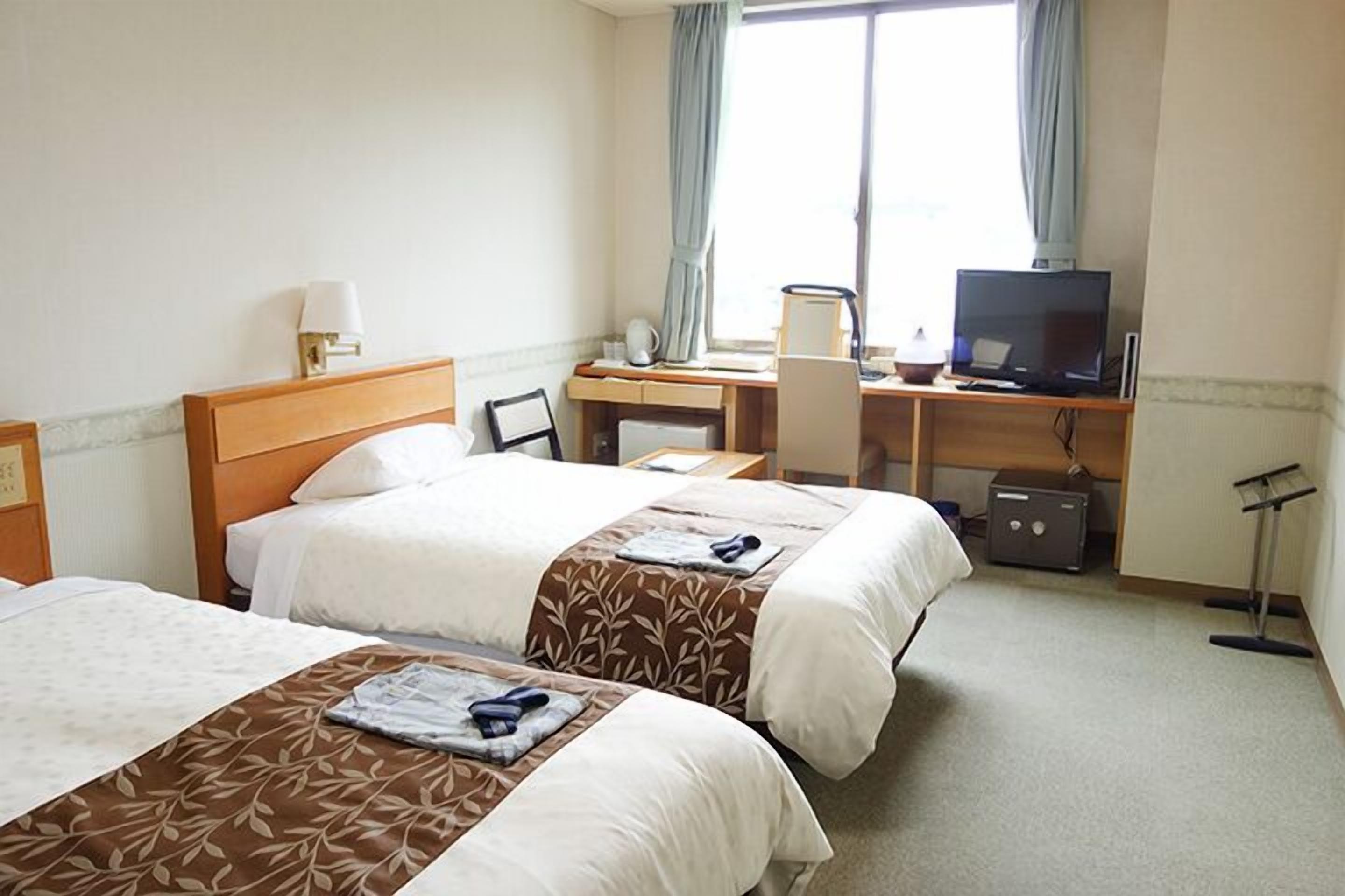 A hotel room with two beds, a desk, a television, and a window with curtains.