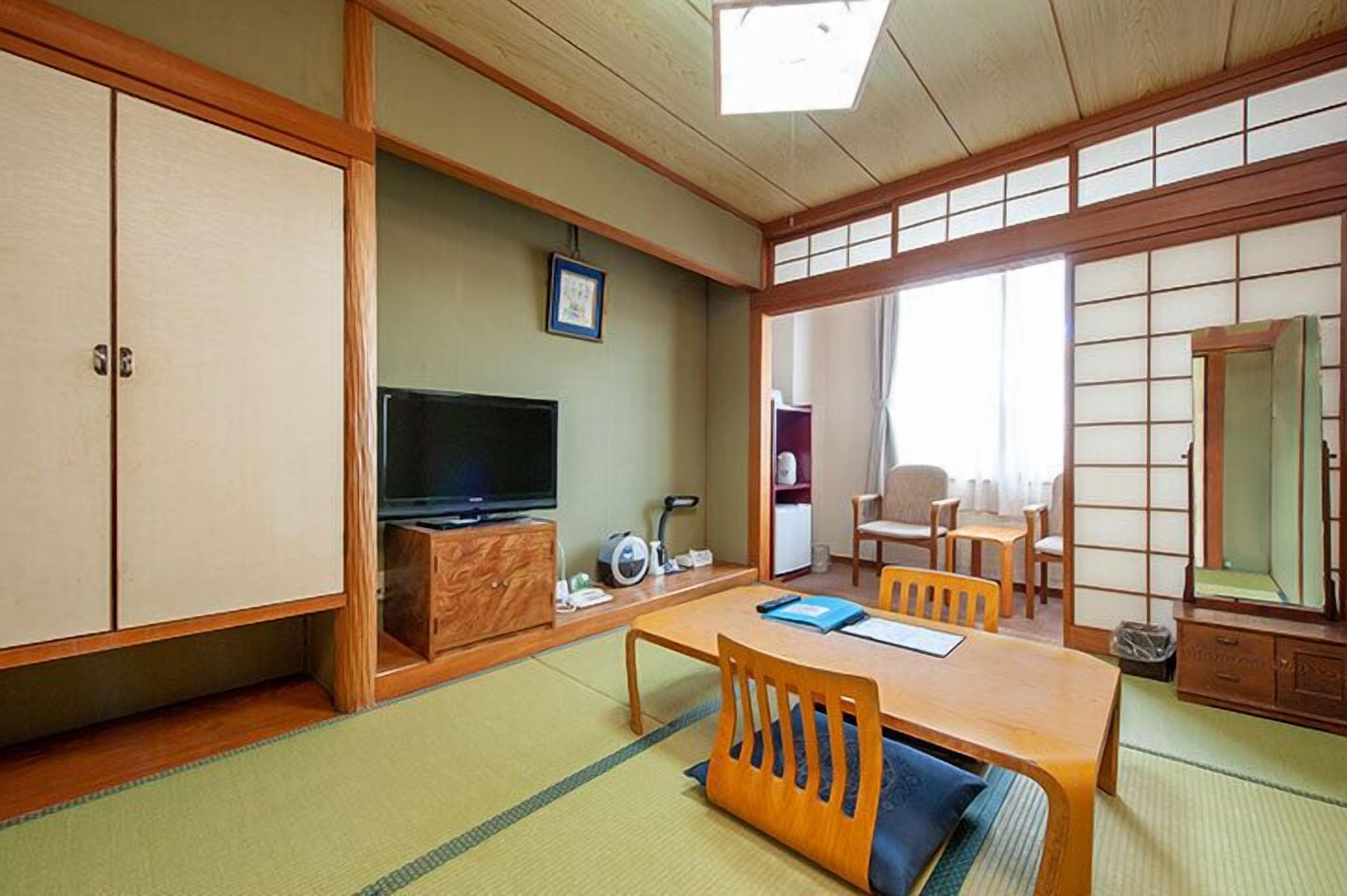 A traditional Japanese room with tatami flooring, a television, a cabinet, and a dining table with chairs.