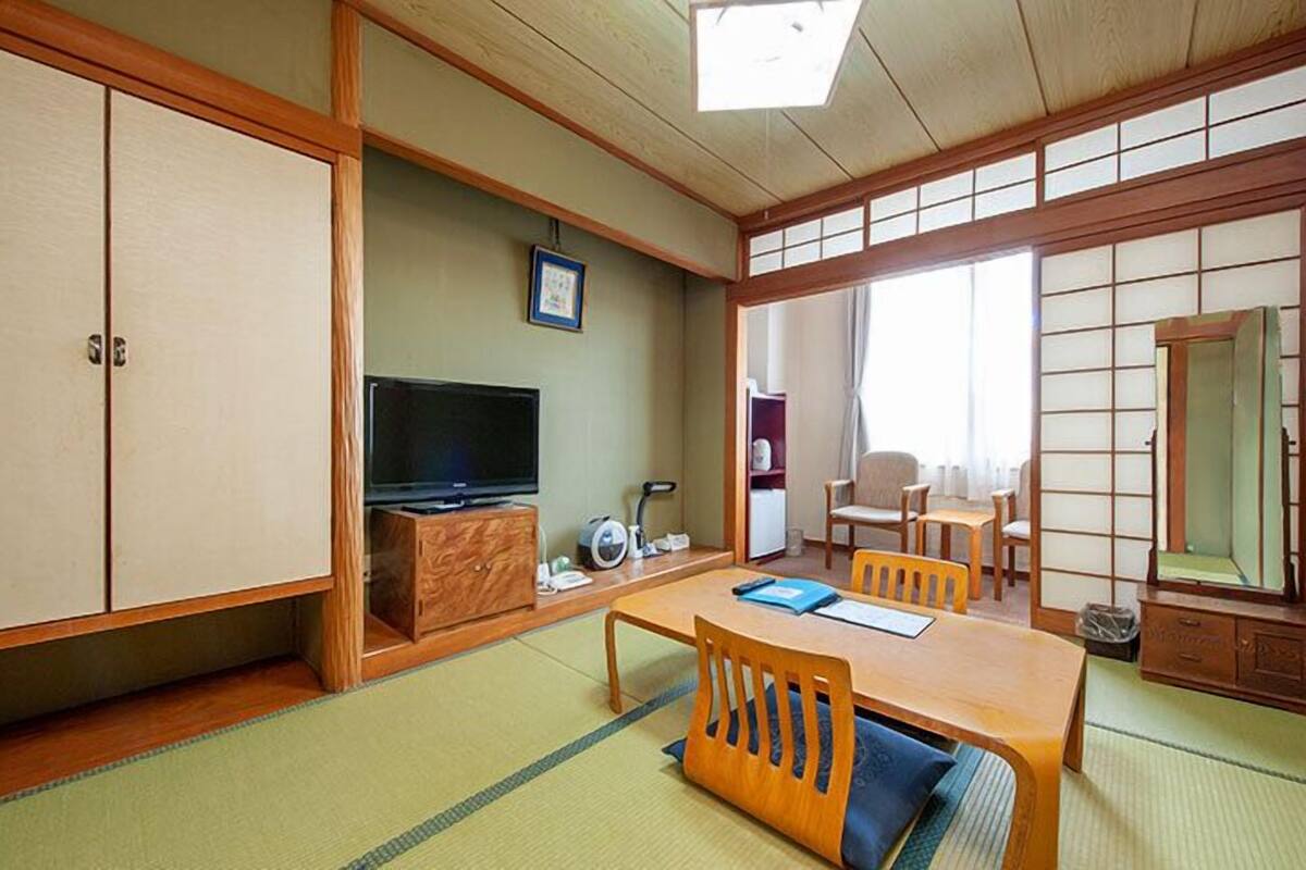 Une pièce de style japonais traditionnel, avec un sol recouvert de tatamis, un téléviseur, un meuble et une table à manger entourée de chaises.